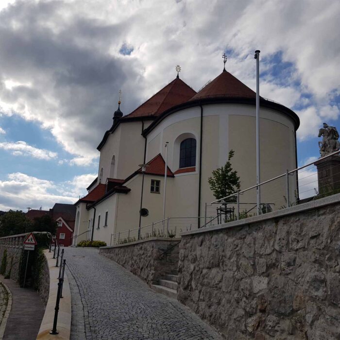 Eine weisse Kirche mit einem hohen Turm steht auf einem Huegel neben einer Strasse